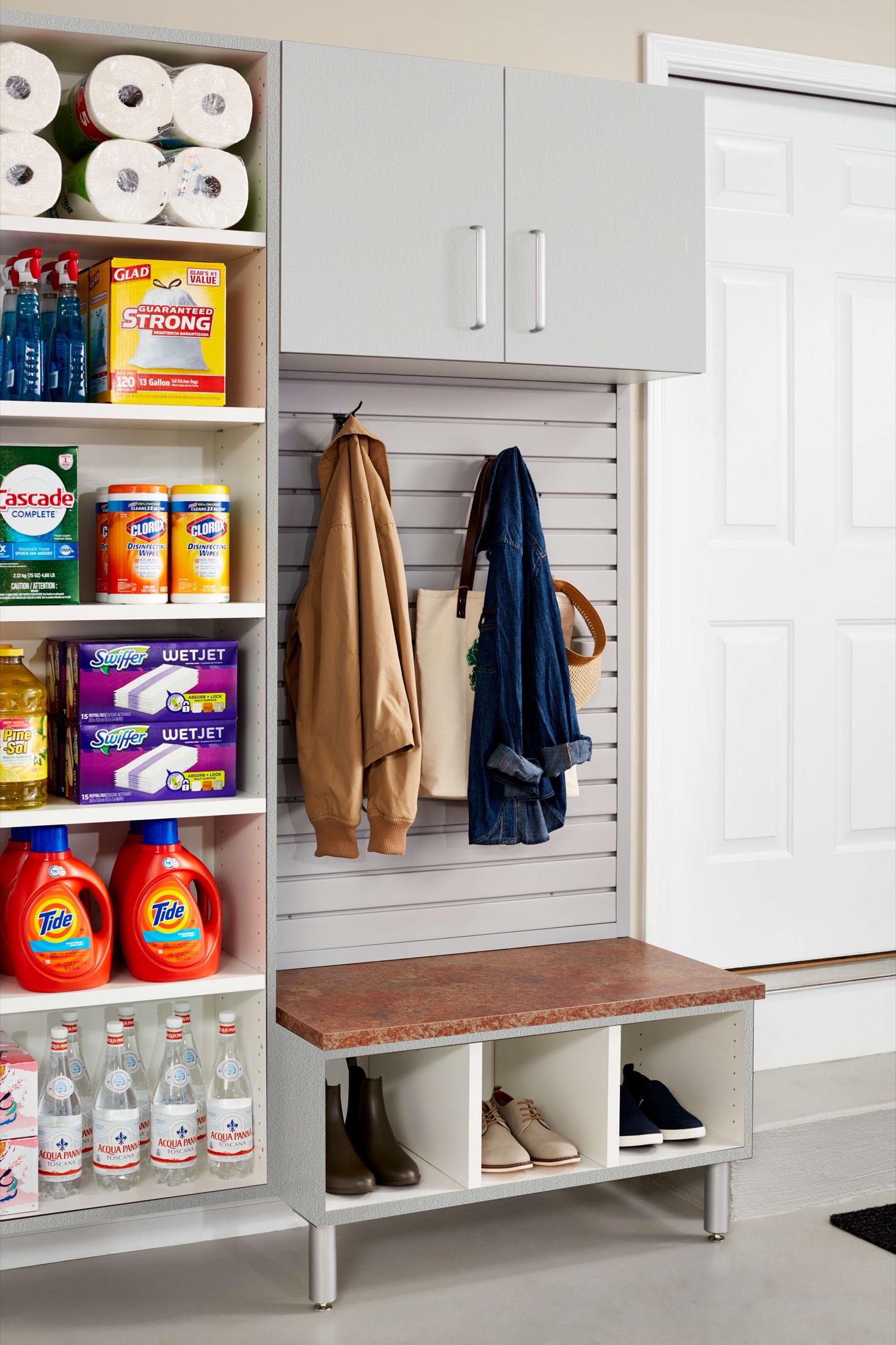 Garage bench with shoe cubbies and coat hooks on slatwall beside a supply shelving tower
