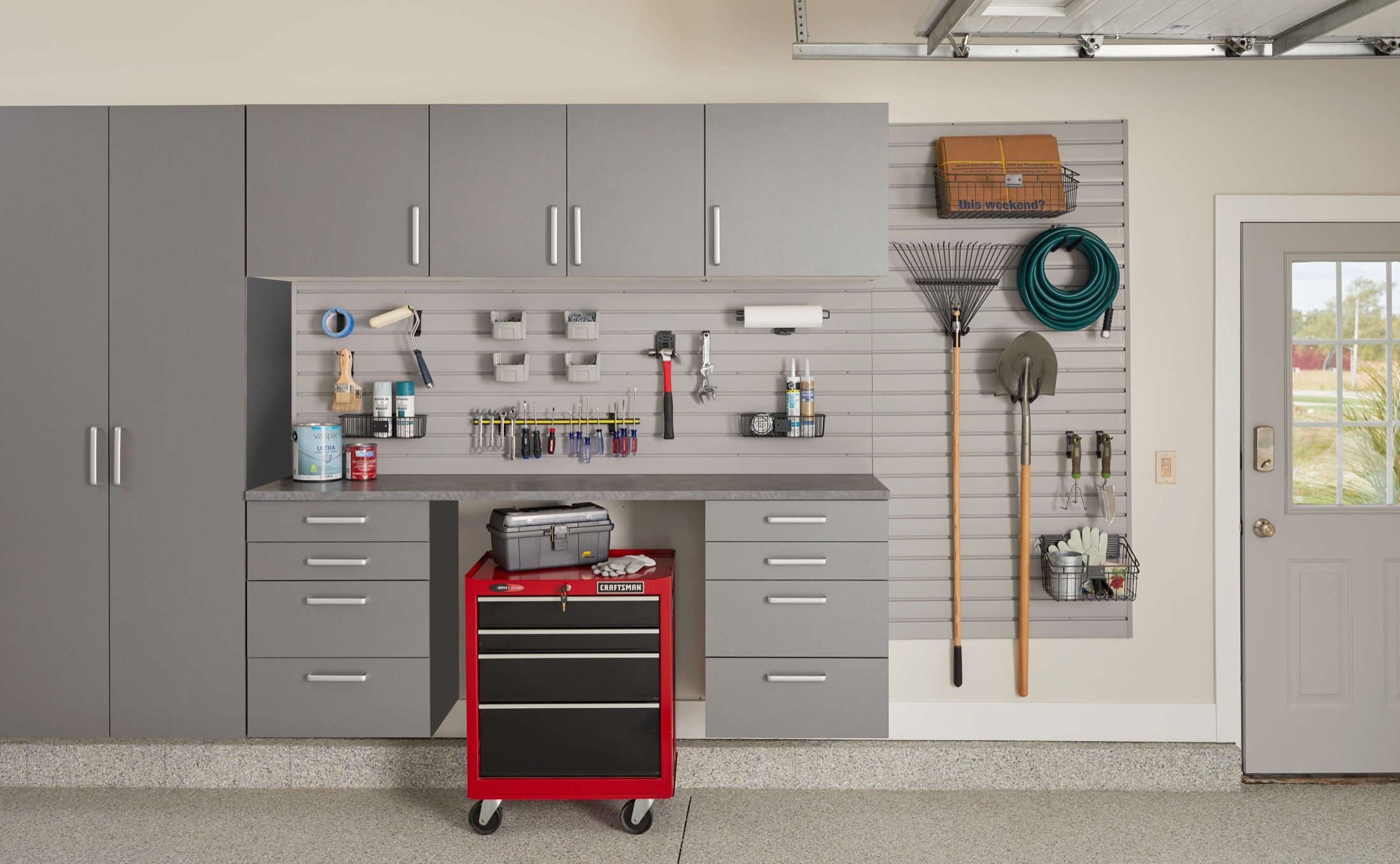 Grey flake garage floor beneath a full wall of cabinets, workbench and slatwall