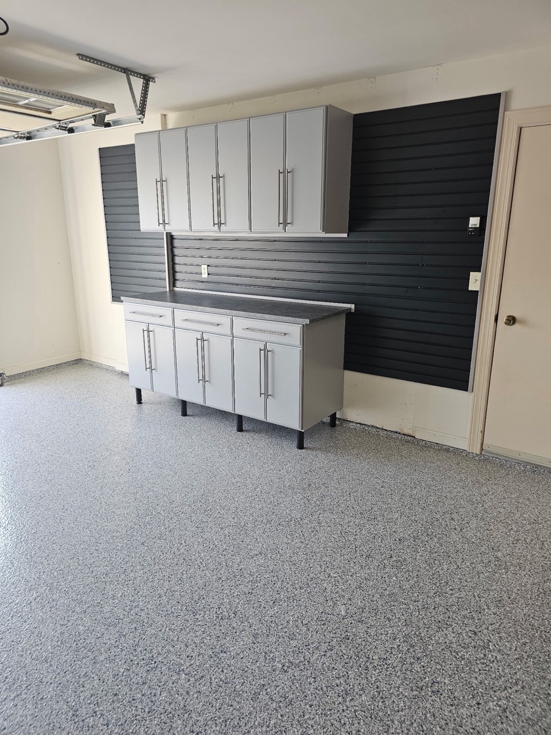 Grey and white flake epoxy garage floor with cabinets and a slatwall behind it